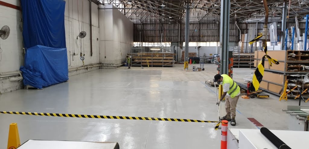 Applicators of Epoxy Flooring Brisbane spreading epoxy paint on industrial warehouse